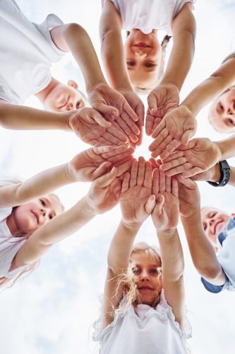 View from below of kids that are holding hands together. Against white sky.
